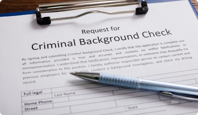 A clipboard holds a Request for Criminal Background Check form. A blue pen rests on the form, which includes spaces for personal information, like name and address. The form emphasizes understanding and consent for checks.